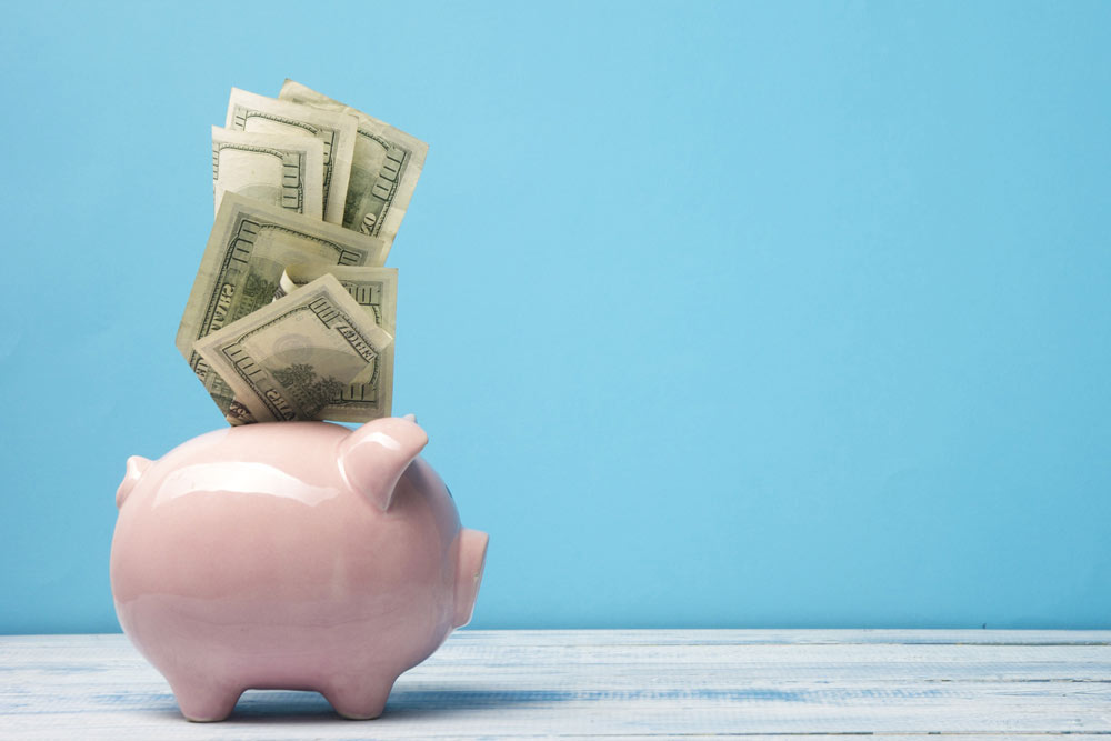 Ein rosa Sparschwein mit Geldscheinen, die aus dem Slot herausragen, vor blauem Hintergrund.