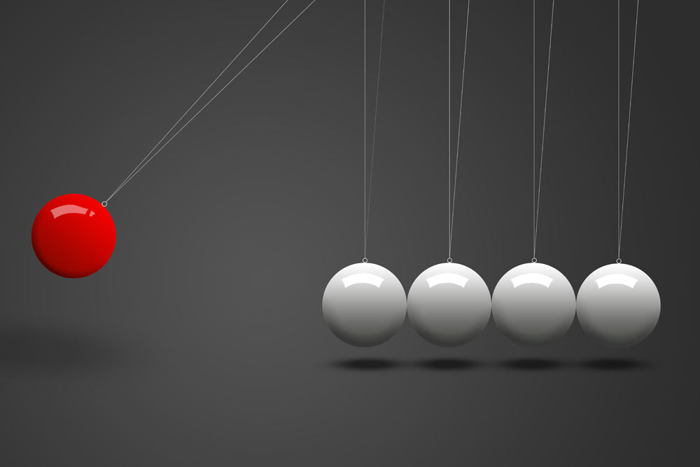 Eine rote Kugel schwingt und beeinflusst vier weiße Kugeln, die an Fäden hängen.