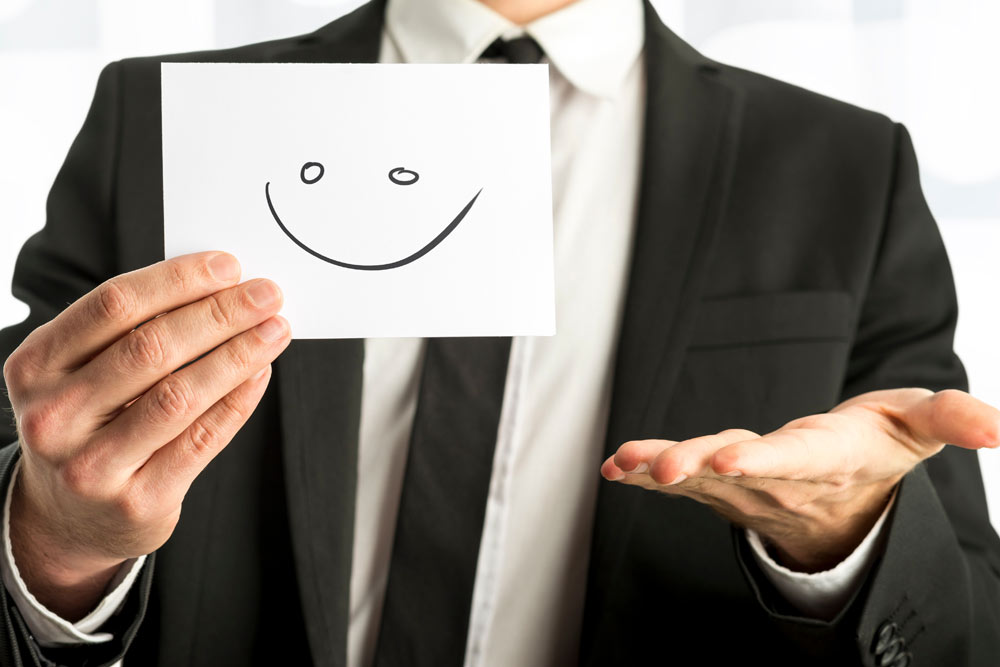 Ein Mann im Anzug hält eine Karte mit einem lächelnden Smiley und einer anderen Hand offen.